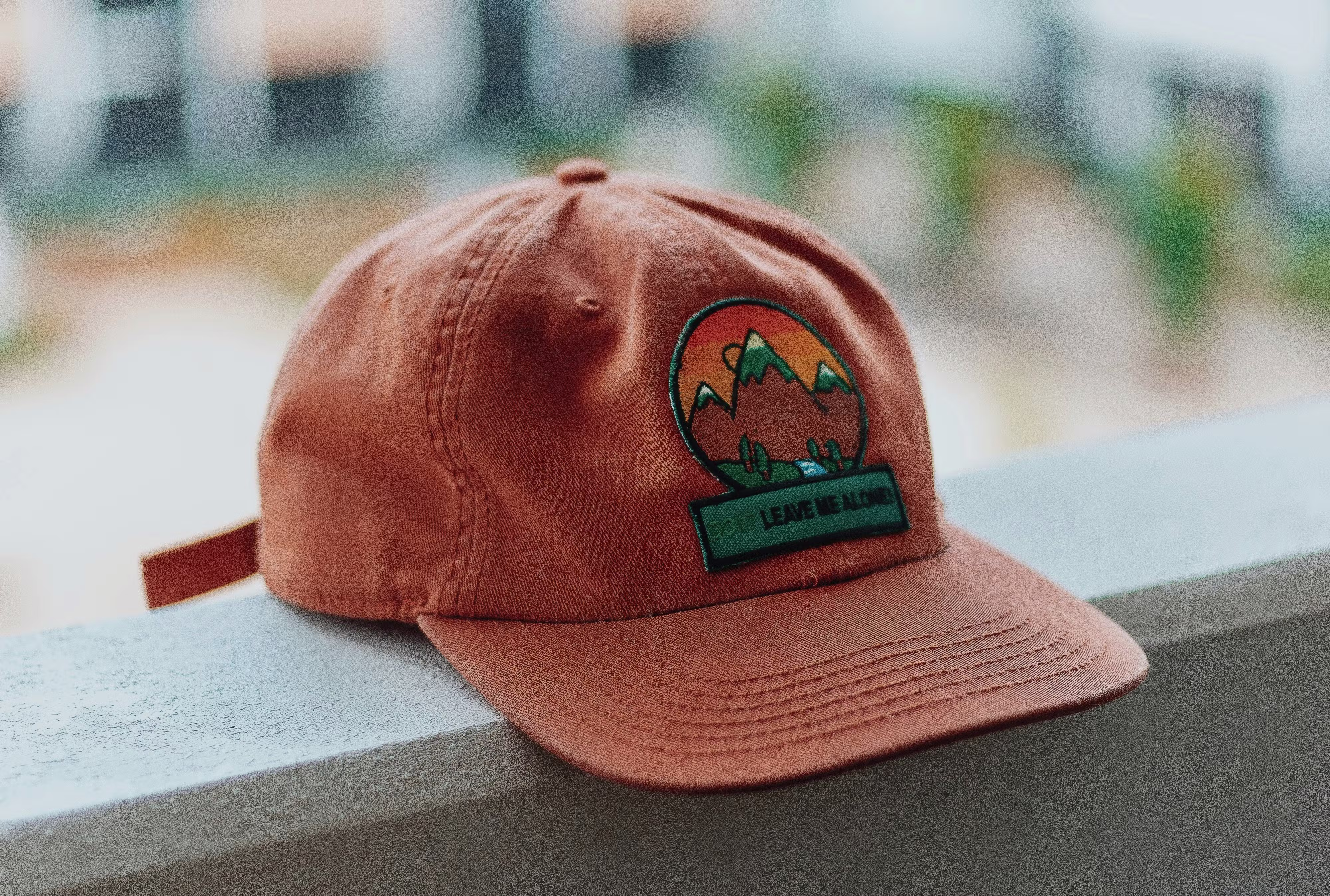 A brown baseball cap with an embroidered patch laying on a white railing